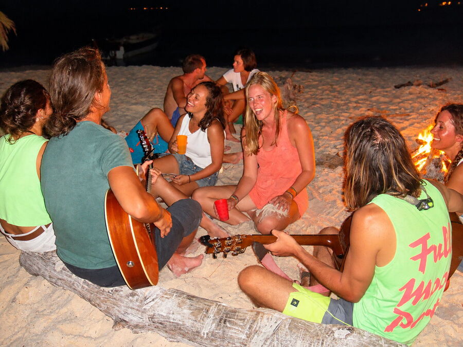 Travelers with guitars around a bonfire on the beach at night